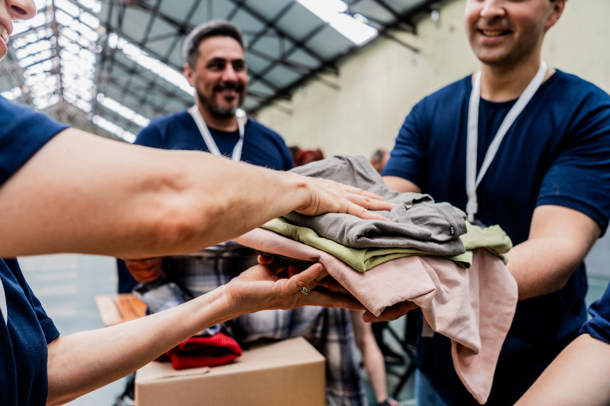 Volunteers passing folded clothing across a donation table.