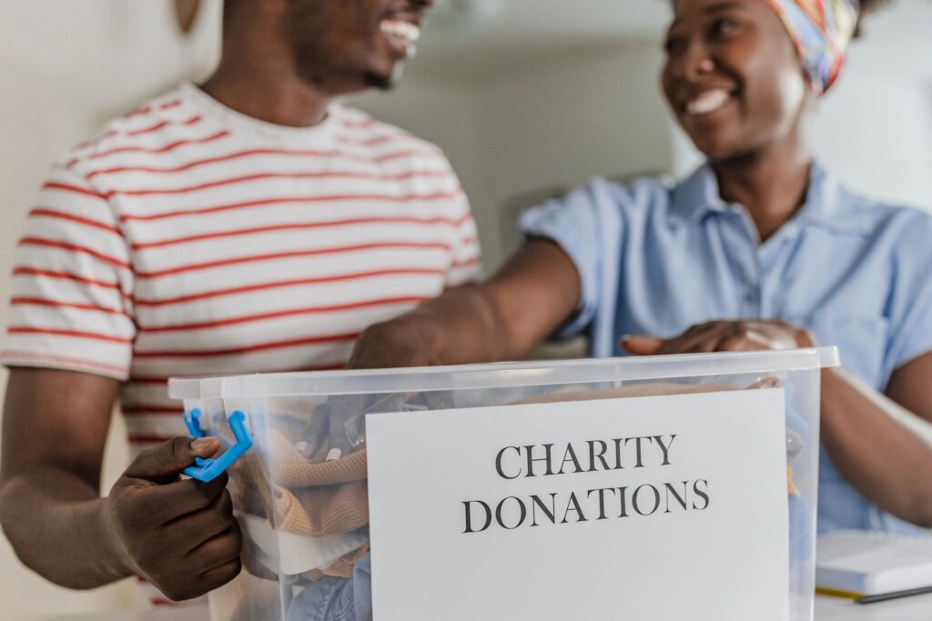 Two volunteers holding a clear box labeled Charity Donations.