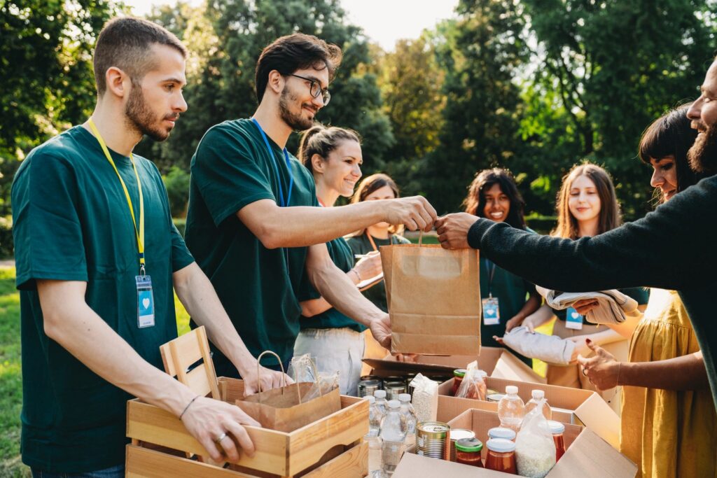 Volunteers handing out a paper bag beside boxes of donated food.