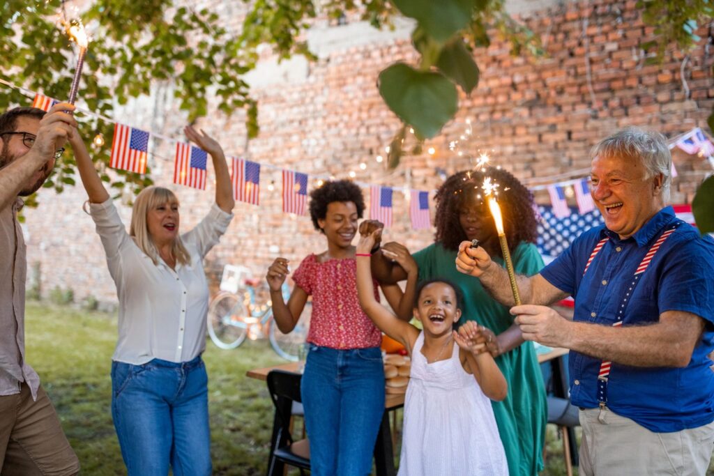 Adults and children celebrating outdoors with red, white, and blue decorations.