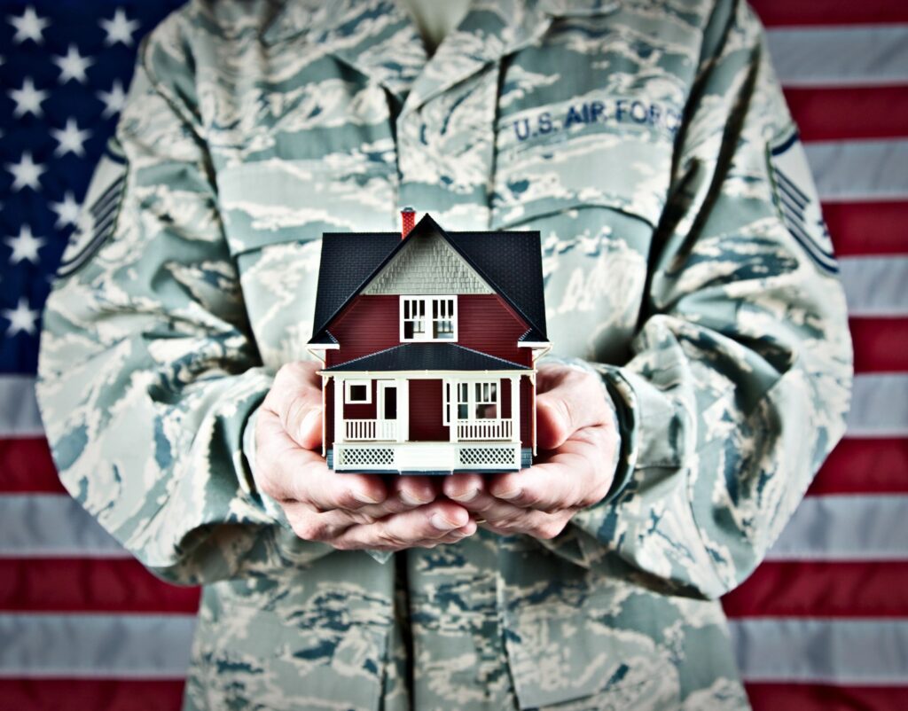 A person in military uniform holding a model house in front of an American flag.