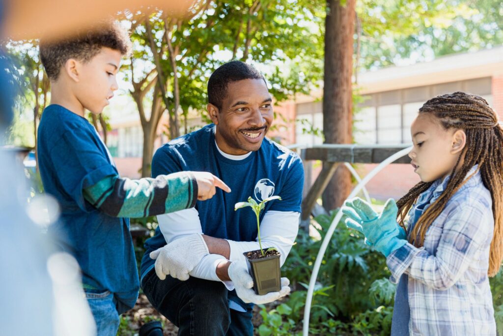 An adult volunteer helping two children with potted plants outdoors.