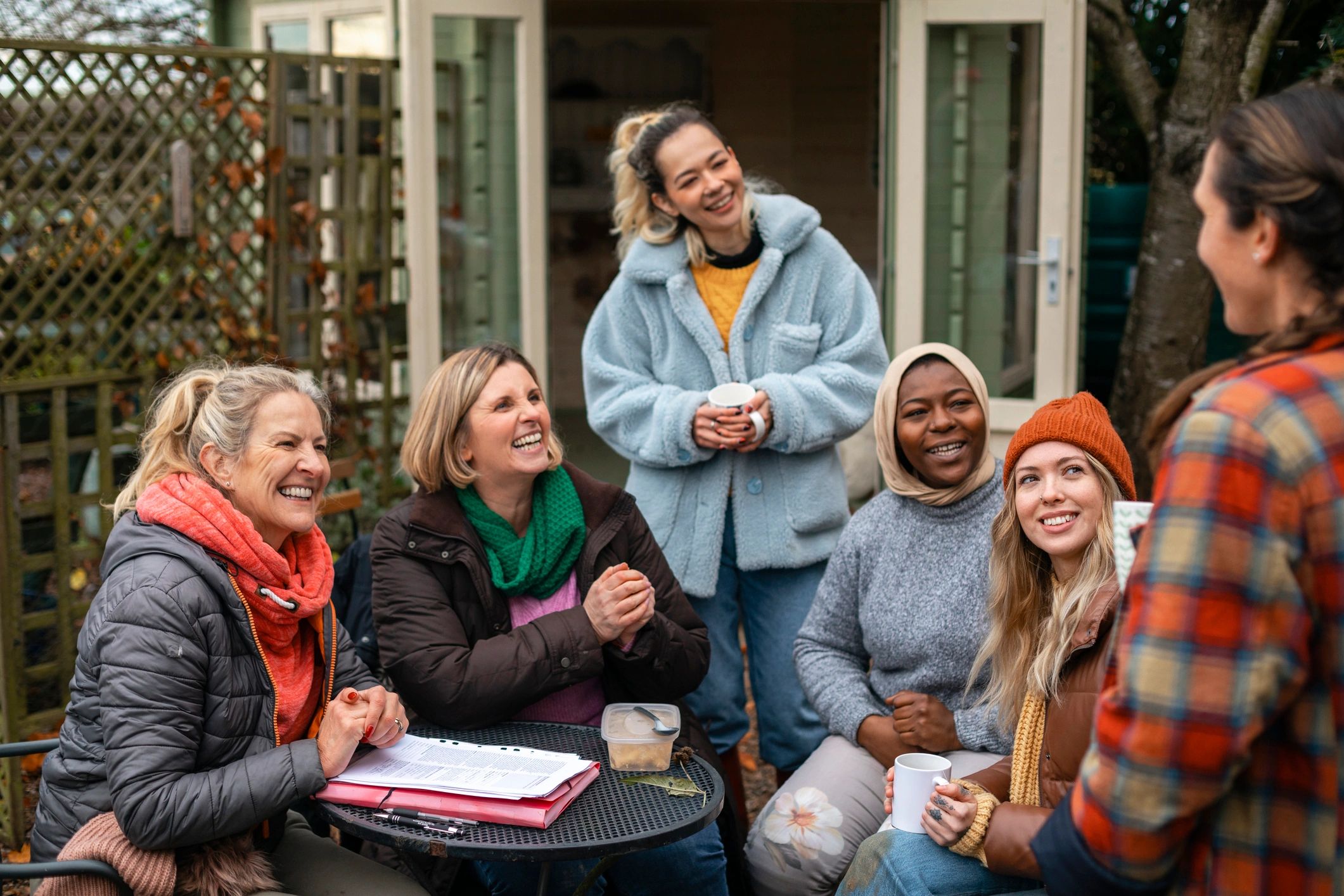 A group of people smiling and talking together around an outdoor table.